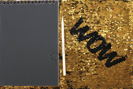 金色亮片背景上黑色亮片的WOW字母和带有黑色床单和木制刮刀的记事本图片