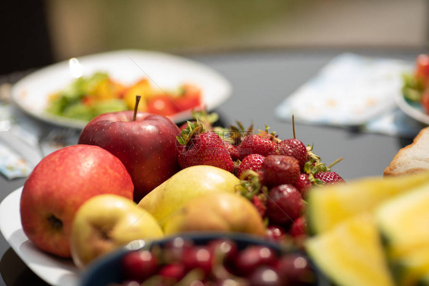 美味的红樱桃站在桌子上的盘子上的特写镜头夏季野餐时供应新鲜水果和蔬菜黄色的苹果和多汁的甜瓜躺在背景上食物和图片