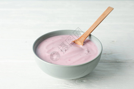 白色木制背景上的碗和勺子中的水果酸奶图片