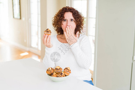 吃巧克力薯片松饼的年长妇女用手把嘴遮住图片