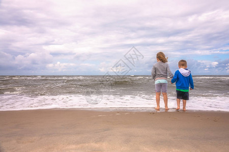 小男孩女站在沙滩上等待夏天海浪到岸边图片