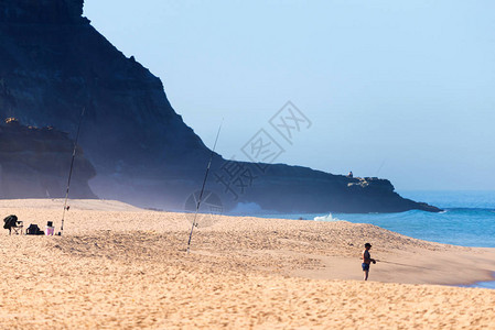 独家渔夫在沙滩上钓鱼杆在海浪倾斜到海边的沙子时图片