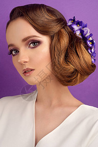 紫罗兰色背景的黑发女郎专业化妆和发型的女孩美容院头发上有蓝色花朵的女孩婚礼发型背景图片