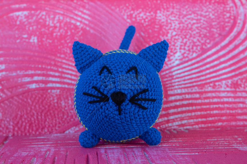 柔软的针织玩具猫圆形的蓝色的颜色在amigurumi的技术中在红色纹理背景上图片