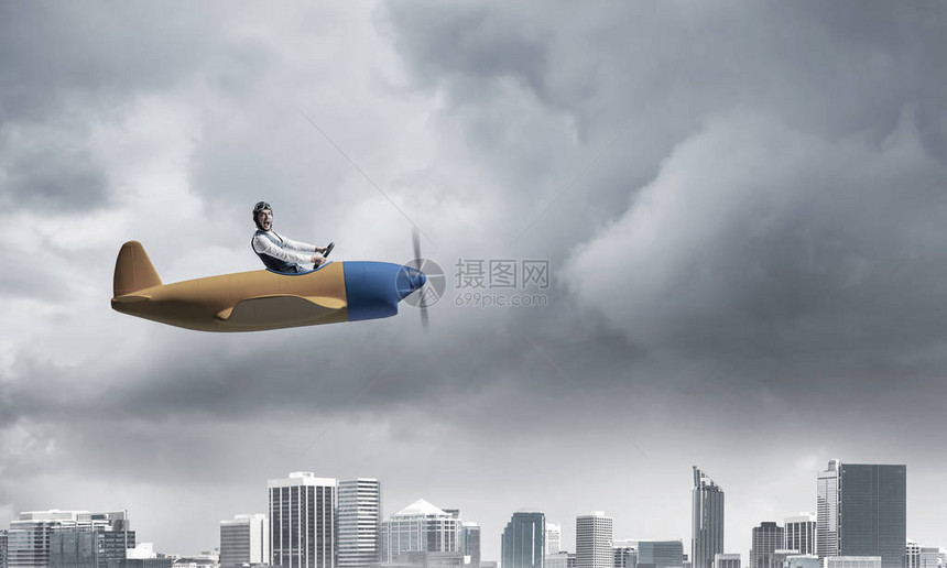 戴着飞行员帽子和护目镜在风暴中驾驶螺旋桨飞机的商人小飞机行员的侧视图大城市全景与戏剧乌云密布的天空景观混合图片