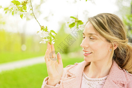 年轻的金发年轻女士在绿公园与开花樱背景图片