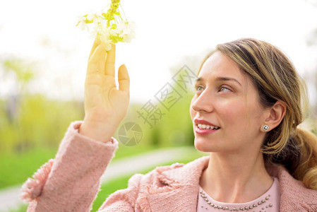 年轻的金发年轻女士在绿公园与开花樱背景图片