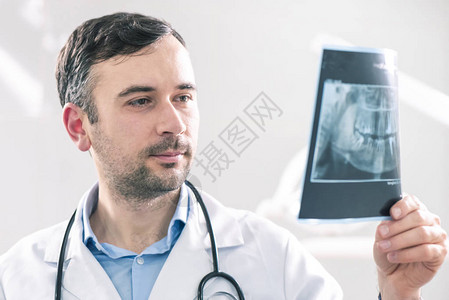 白种男牙医分析牙科柜的X光片近镜头白色孤立背景从背面闪亮图片