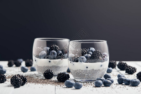 在散落在散落的种子蓝莓和黑莓附近的玻璃杯中图片