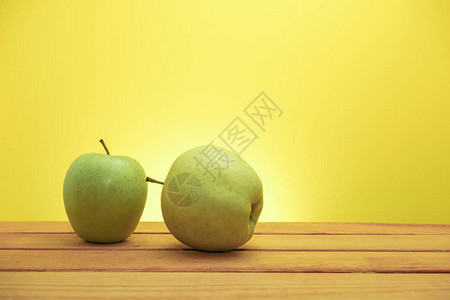 红色木桌上的两个青苹果黄色背景图片