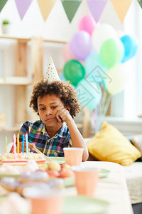 虎年生日肖在生日派对期间独自坐在桌边的非洲美国男孩的悲惨肖背景