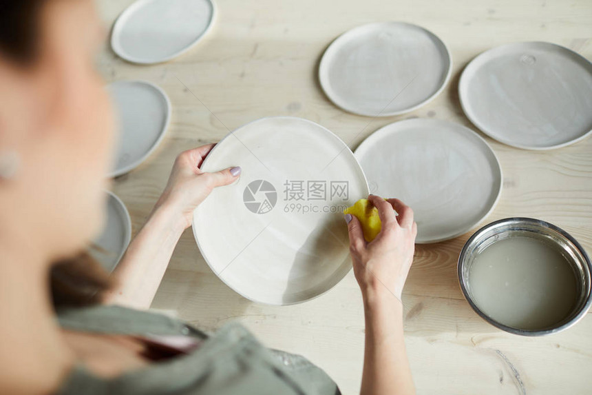 无法辨认的年轻女子在陶瓷车间复制空间完成手工制陶瓷板的高角图片