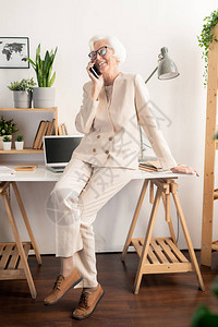 身穿优雅白色西装的高级快乐女坐在办公桌上图片