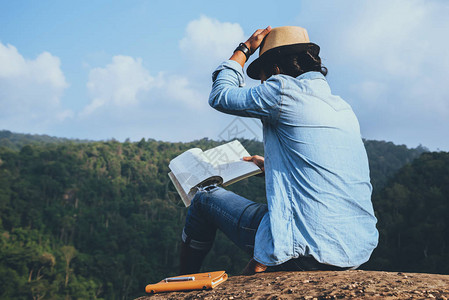 亚洲人旅行在假期放松座位放松在岩石峭壁上看书在图片
