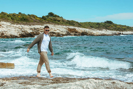 男子在寒风的暑假中走在岩石海滩图片