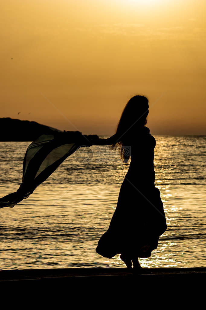 美丽的女剪影无法辨认的苗条高个女人与丝巾在金色的爱奥尼亚海水前夕阳从阿尔巴尼亚卡萨米尔看到的五颜六色图片