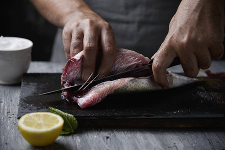 一个年轻的白人男子用刀在石板托盘上切割生鲜鲭鱼的特写图片
