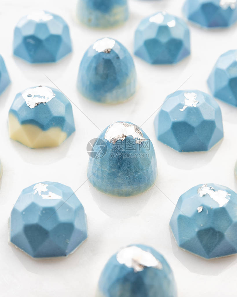 白大理石背景上涂有蓝漆和银泡子的豪华手工制巧克力糖果图片