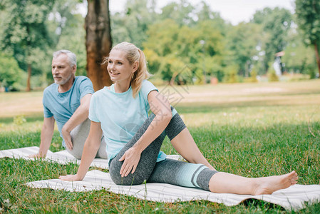 坐在公园瑜伽垫子上做瑜伽的成熟笑图片