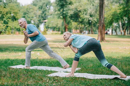 成熟的男人和女人站在公园的瑜伽垫上练习瑜伽图片