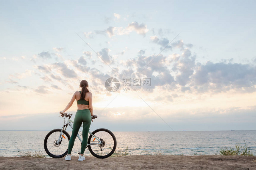 一位美丽的年轻黑发女子在日出时骑自行车后休息的肖像早上听无线耳膜音乐的模特儿图片