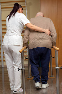 年轻护士用平行衡杆辅助中风患者的全长后视图老人在诊所的前传图片