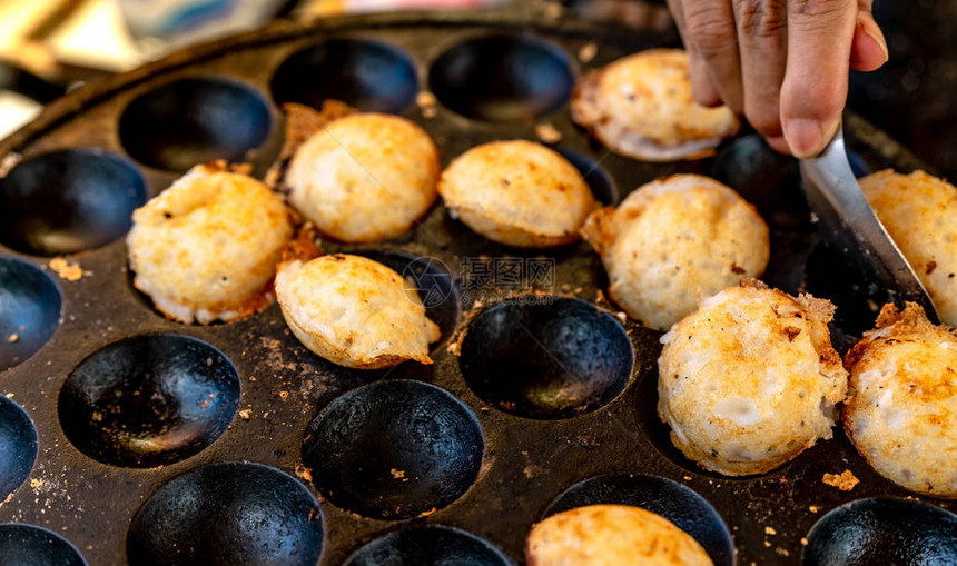砂浆烤糕点或KanomKrok是泰国传统甜点女人用手勺子从炉子里取出KanomKrok泰国街头小吃由椰奶和面粉制图片