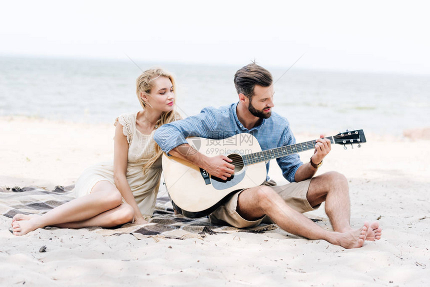 坐在毯子上与男友一起坐在海边滩玩音响吉他的美丽的图片