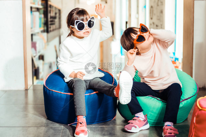 新时尚太阳镜安静的患有唐氏综合症的年轻姐妹们在扶手椅上休息时穿图片