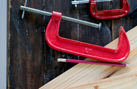 用铅笔和其他设备放在木桌上的用于木工作的红色夹具工图片