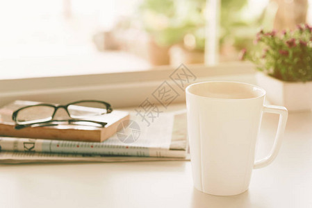 上午咖啡带报纸眼镜书本和花盆的咖啡杯放在窗户图片