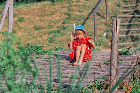金发碧眼的小女孩穿着圆点红裙赤脚走在木桥上图片