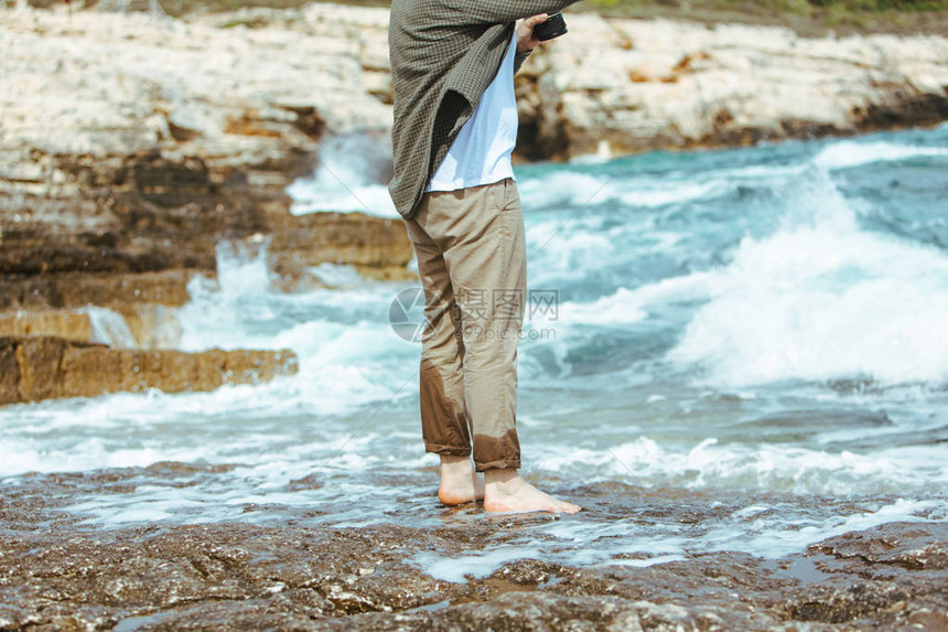 湿脚穿裤子的男子在海边岩石海滩上图片