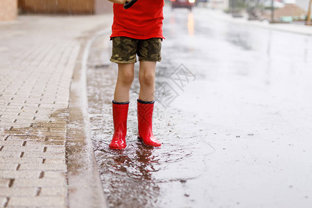 穿着红色雨靴的孩子跳进水坑特写孩子玩得开心泼水温暖的夏雨背景图片