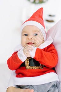 一个穿着圣诞老人套装的五个月大的小孩躺在父母的手上图片