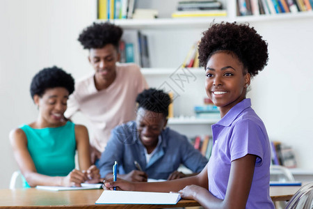 笑非洲裔美国女学生在学校的办公桌上与老师和一群学生图片