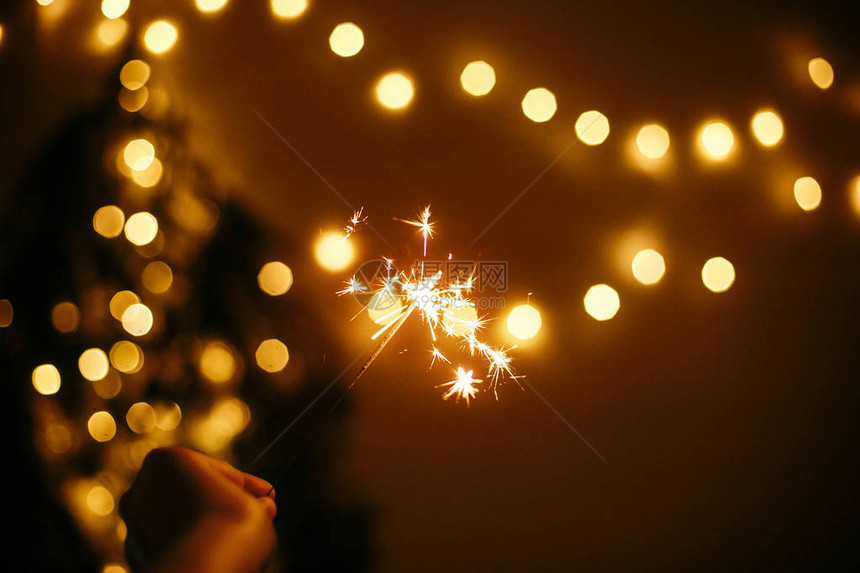 手握着金色圣诞灯背景上闪发光的火花图片