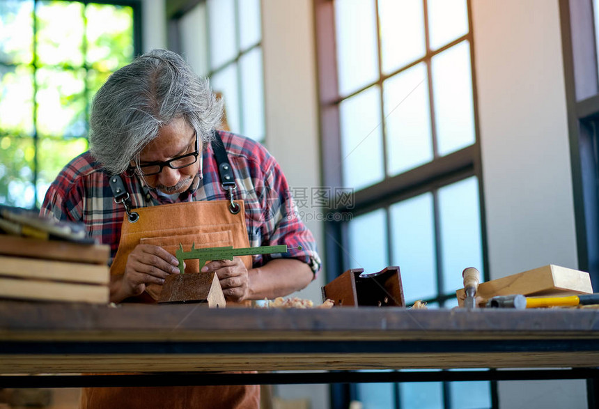 亚洲老手工匠白天利用卡利珀斯帮助在室内使用木制品图片