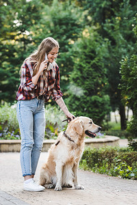 穿着休闲服的漂亮年轻女孩带着金毛猎犬在公园里醒来图片