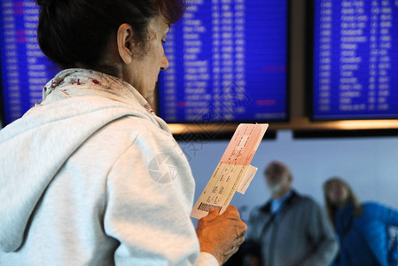 有票的老年妇女正在寻找时间表上的航班日程安排图片