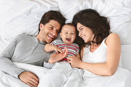 白种人的母亲父亲和婴儿在床上与婴儿一起醒来图片