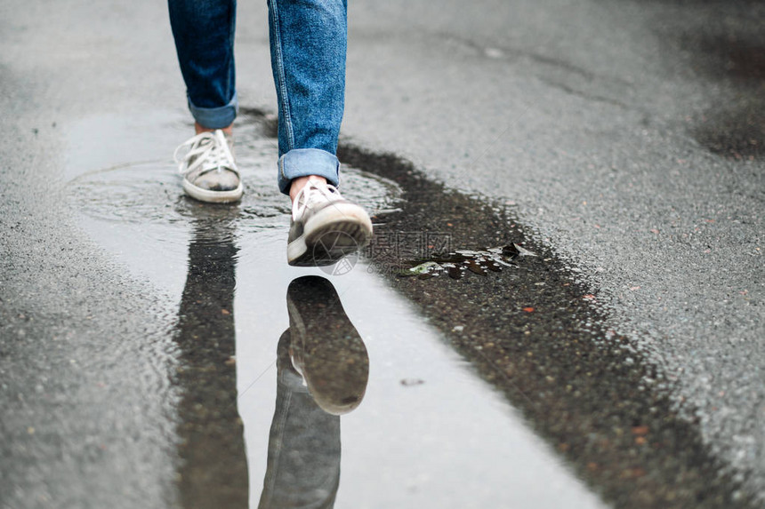 穿着运动鞋的近脚穿行在人行道上的水坑中雨图片
