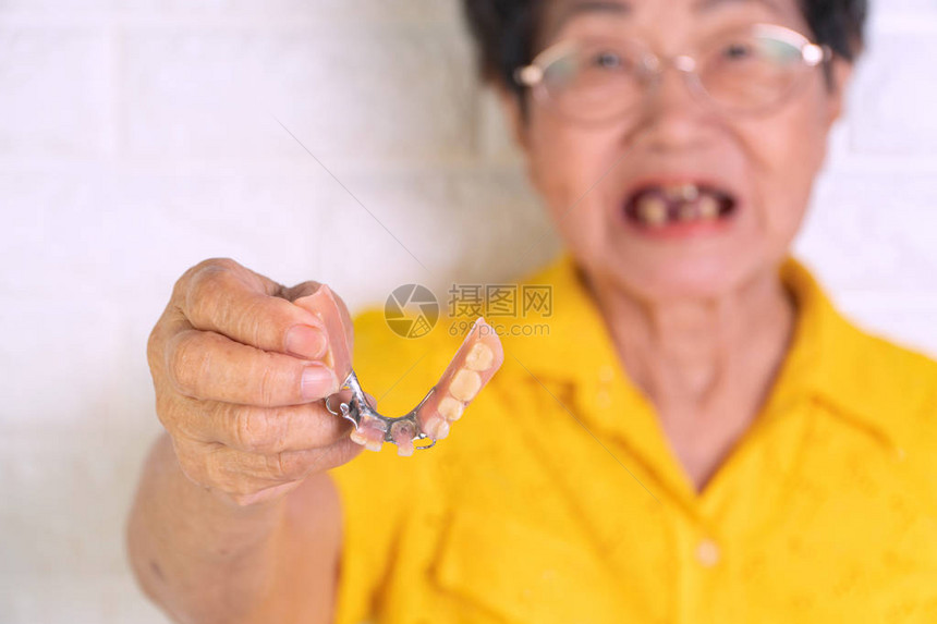 70多岁的亚洲老年妇女手拿假牙用于修复缺失的牙齿并帮助咀嚼的假牙老年人咀图片