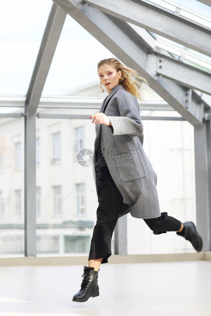 穿着灰大衣黑裤子黑色脚踝靴子和金耳环的年轻优雅女子图片