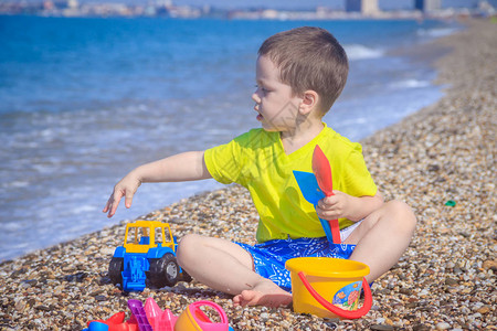 小男孩在小石头沙滩上玩耍带着丰富多彩的玩具图片