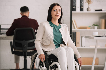 坐在轮椅上的残疾女商人在后台工作的同事附近微图片