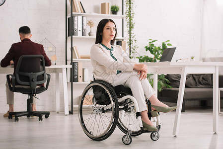 坐在同事附近办公室轮椅上担任职务的残疾严图片
