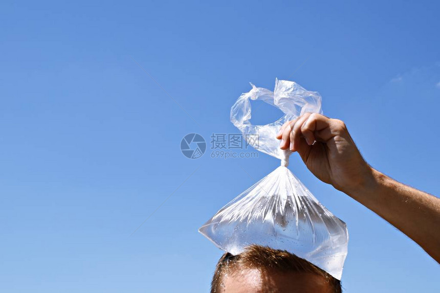 一个二十多岁的男人在没有云的湛蓝天空前用装满冷水的塑料袋冷却头欧洲炎热夏图片
