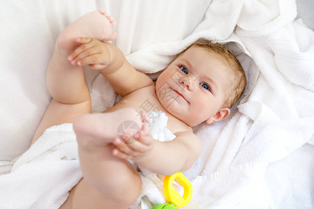 可爱的小宝洗澡后玩具拨浪鼓和自己的脚可爱的漂亮女孩裹着白毛巾快背景图片