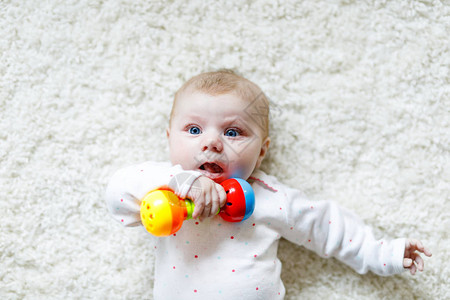 可爱的新生婴儿在白色背景上玩五颜六色的拨浪鼓玩具图片